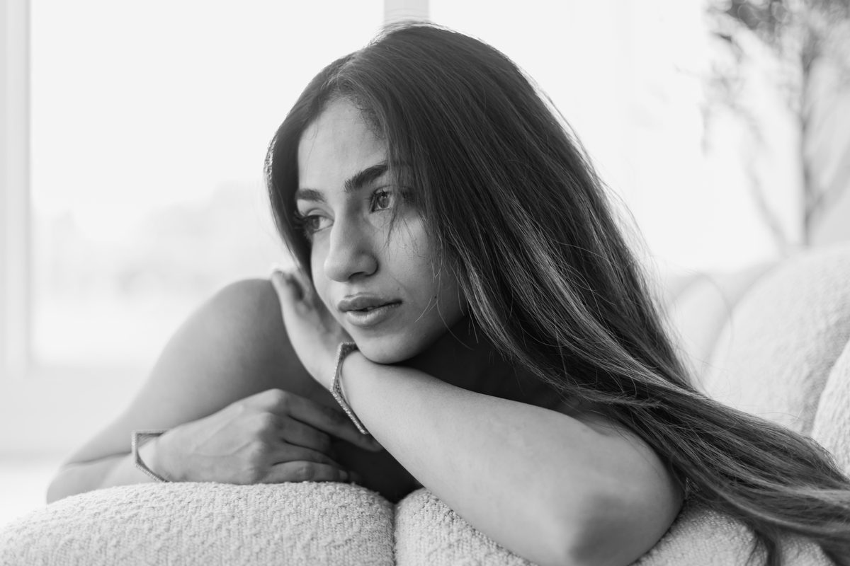 Black and white portrait of a woman resting her chin on her hand beside a bright window, soft directional light across her face