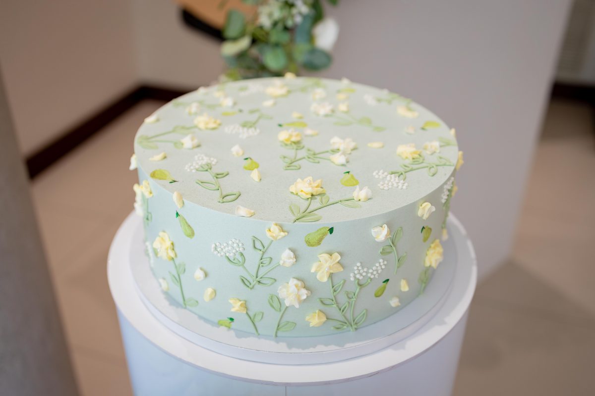 Close detail of a pale green bridal shower cake hand-piped with small yellow and white flowers