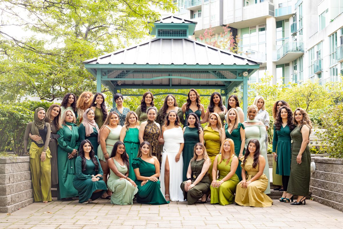 Large bridal shower group photograph of guests in green and gold dresses gathered around the bride outside a garden gazebo