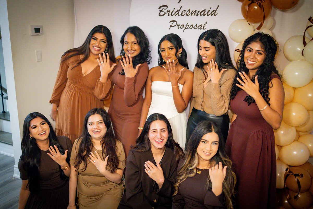 Group photograph of the bridal party in brown and rust tones holding their hands up together in celebration