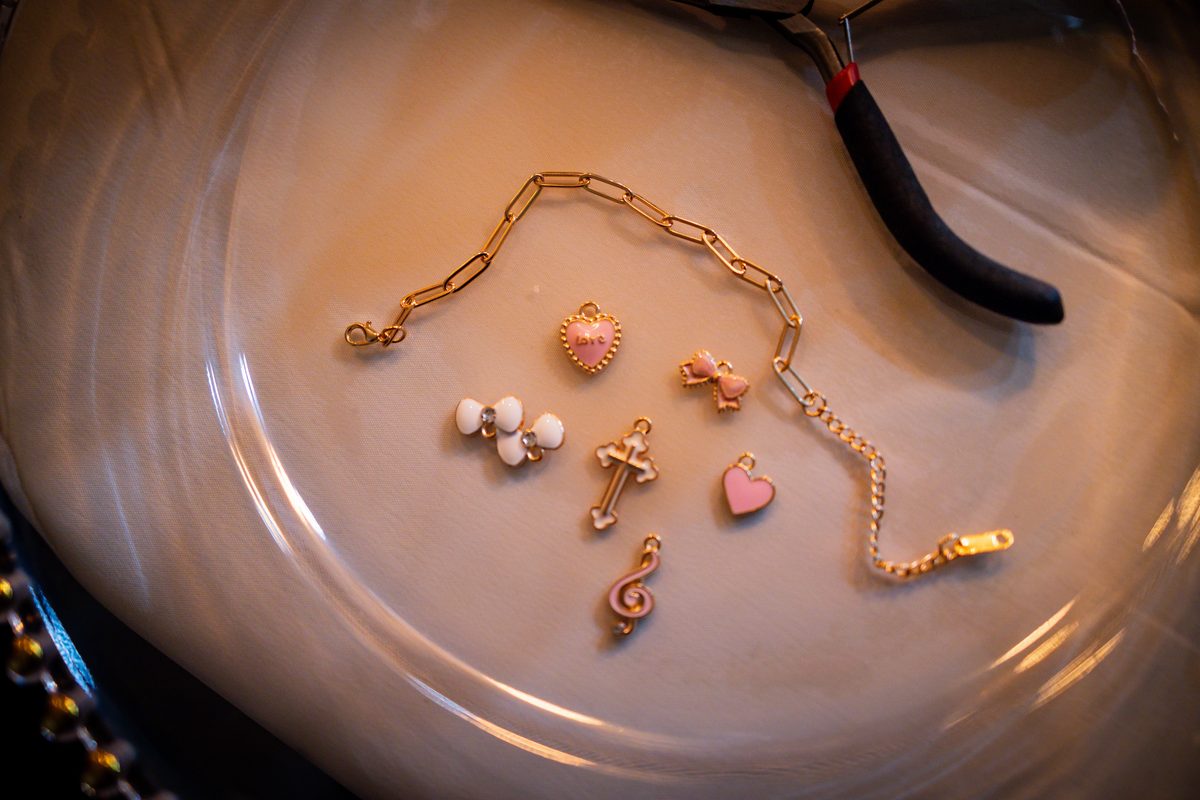 Detail flat lay of a gold charm bracelet with pastel enamel charms laid out on a warm beige surface