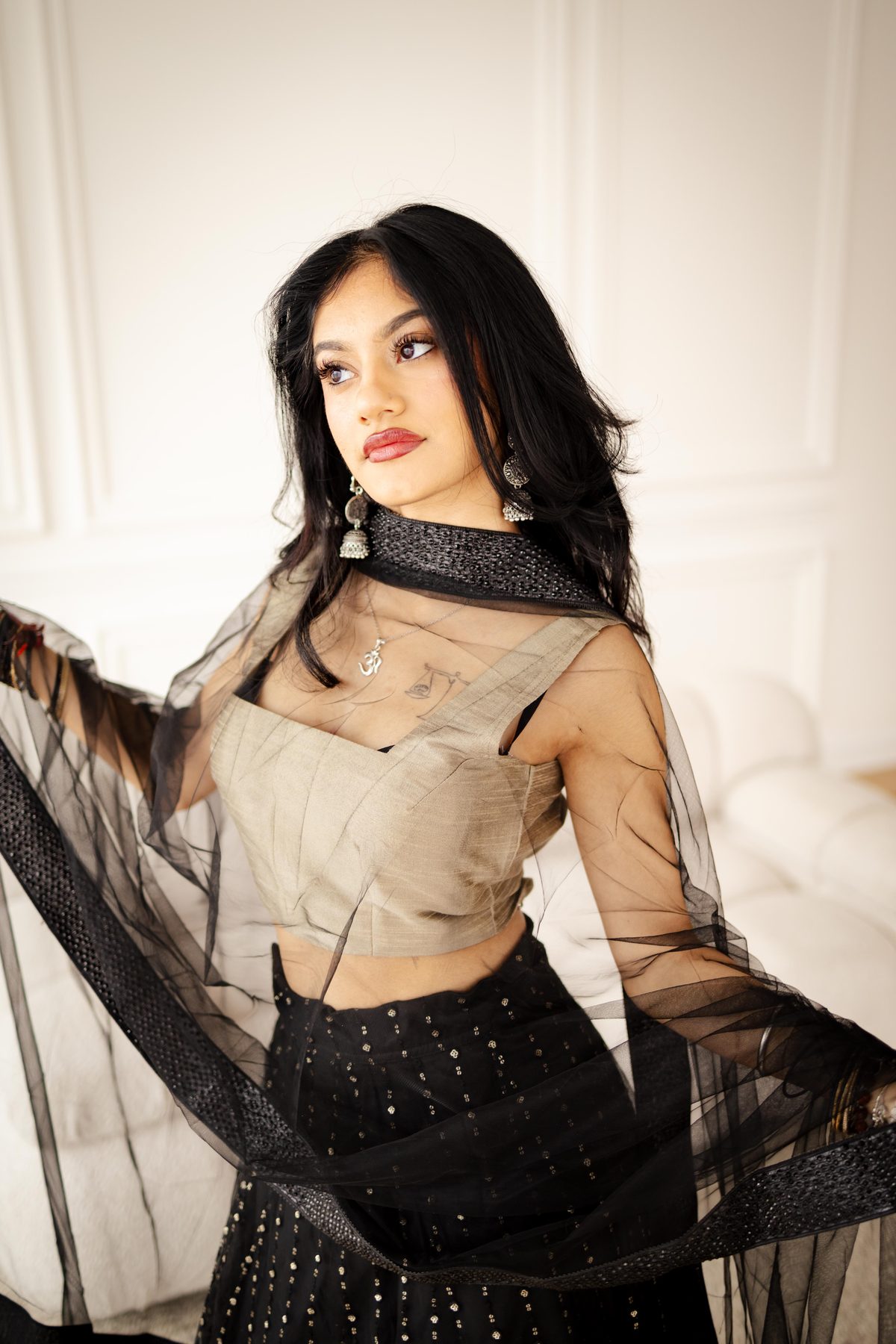 Portrait of a woman in a sheer black and gold outfit, backlit by window light in a bright panelled room