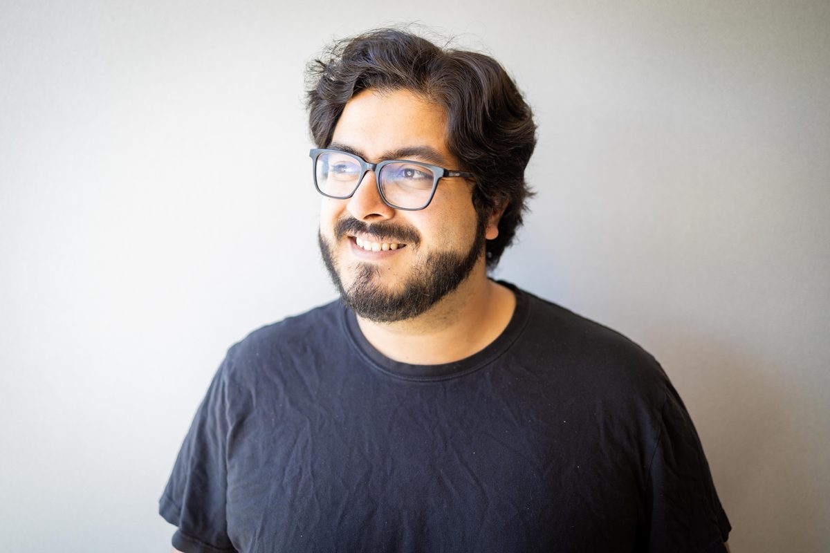 Relaxed LinkedIn headshot of a bearded man in glasses and a dark t-shirt against a seamless grey studio backdrop