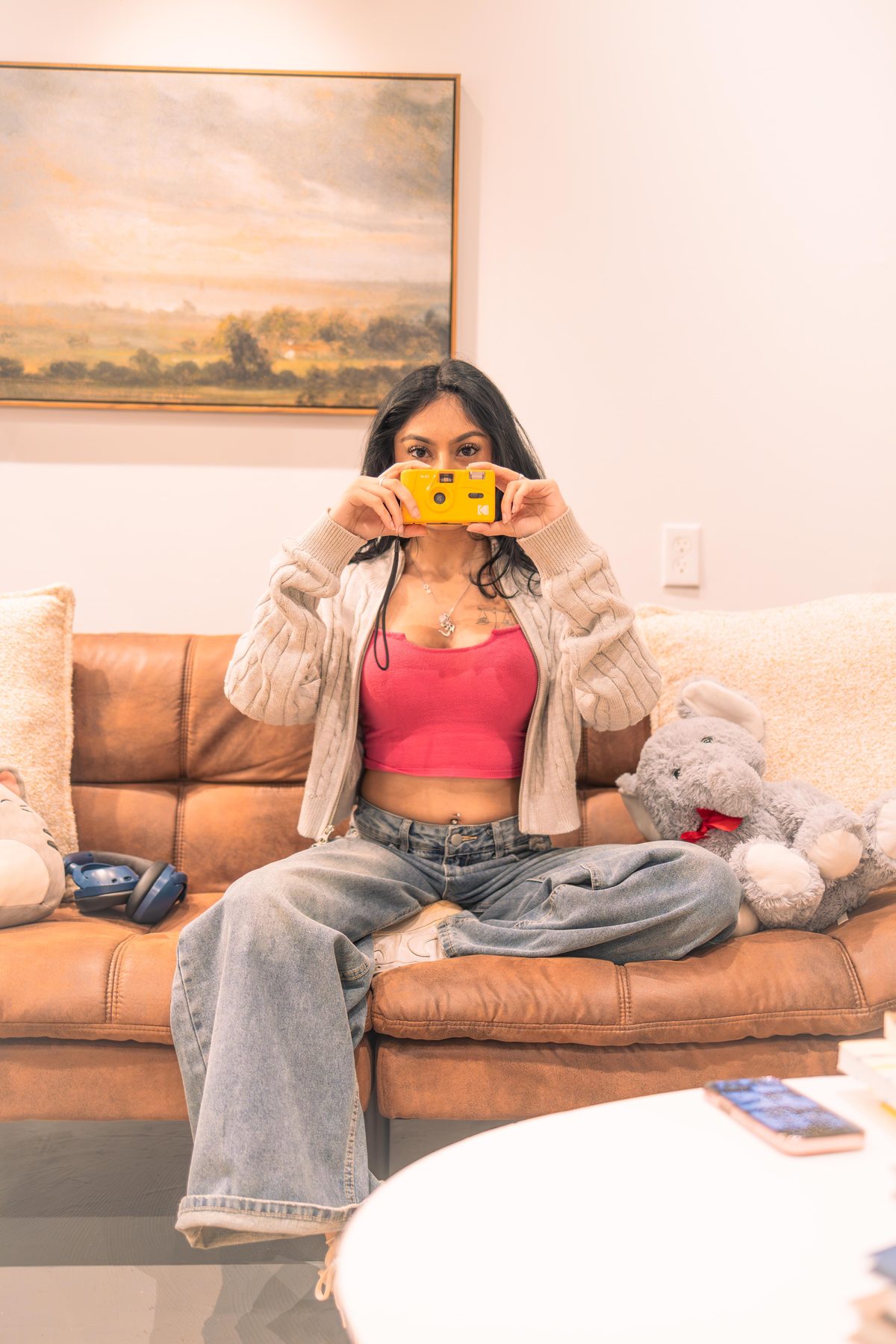 Playful lifestyle portrait of a woman on a couch holding a small yellow film camera up to her face