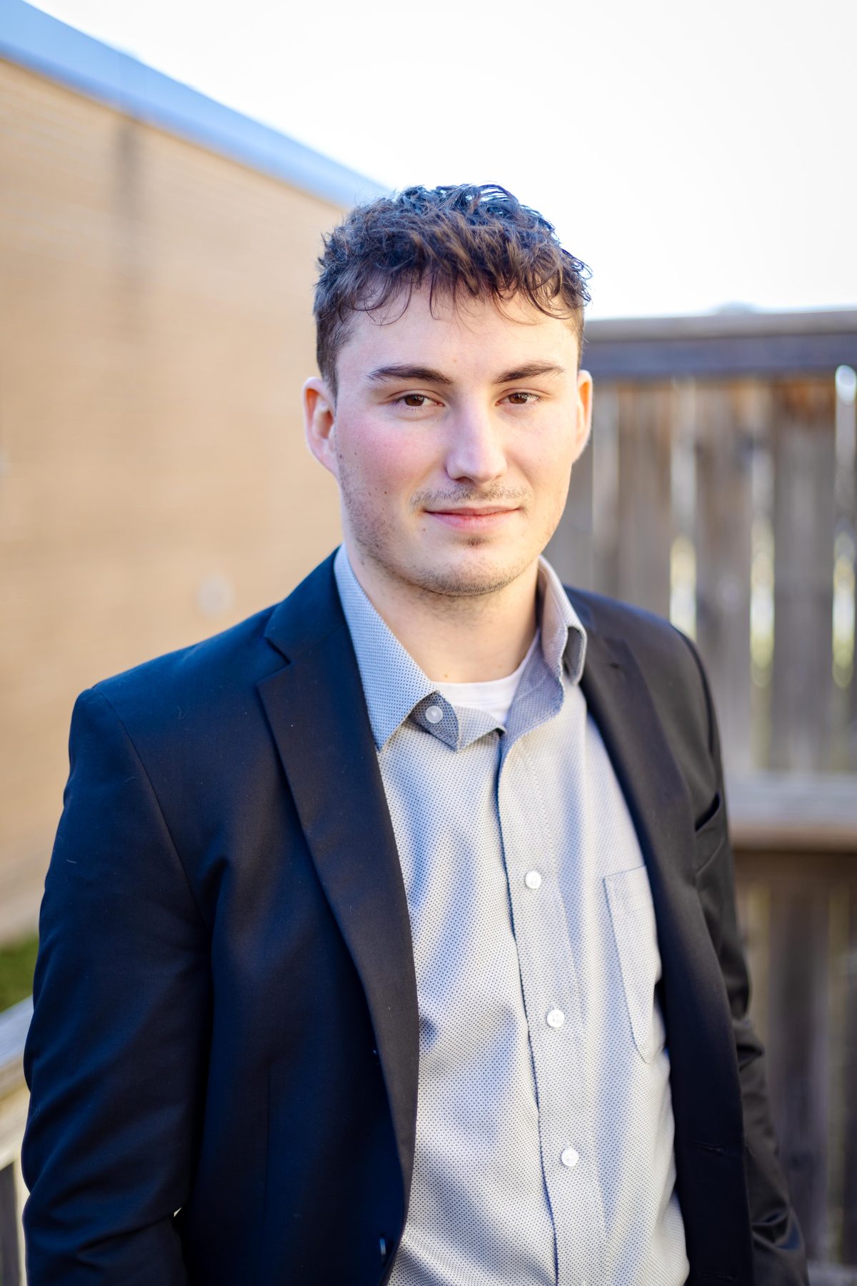 Professional headshot of a young man in a navy suit jacket and light dress shirt, photographed outdoors in natural light in Mississauga