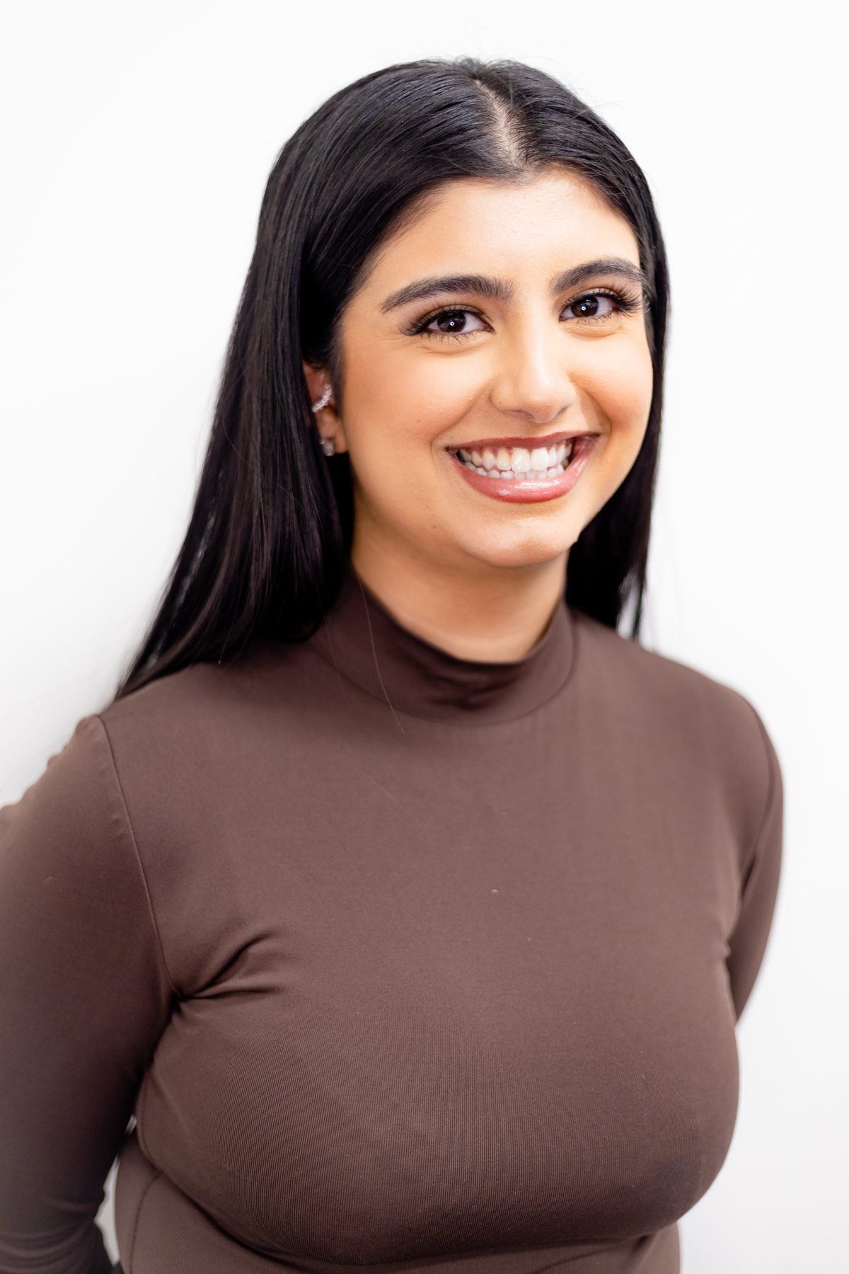 Studio headshot of a smiling young woman in a brown turtleneck against a clean white backdrop